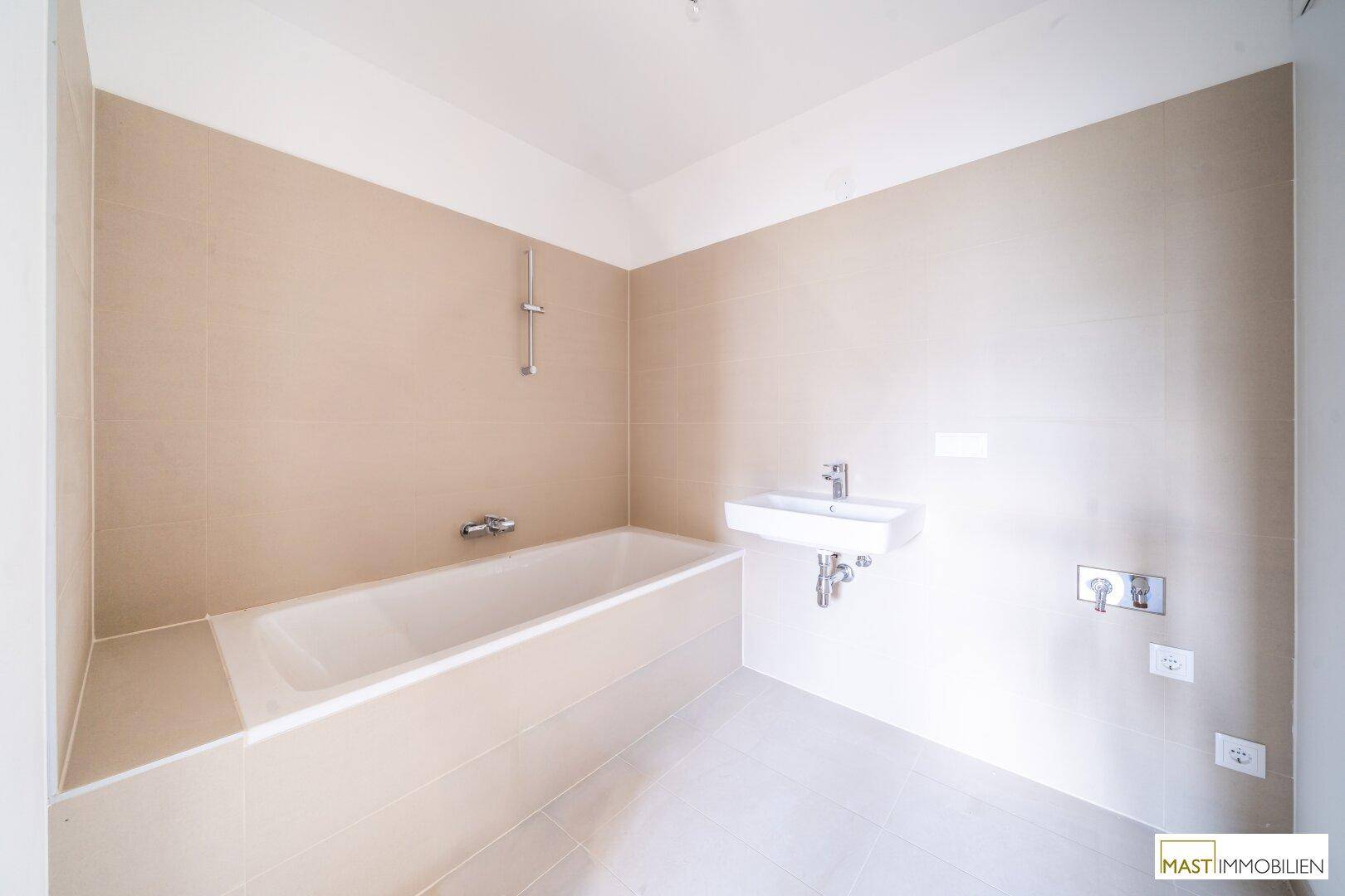 Modernes Badezimmer mit Badewanne und Einzelwaschbecken, hell gefliest in Beige- und Grautönen.