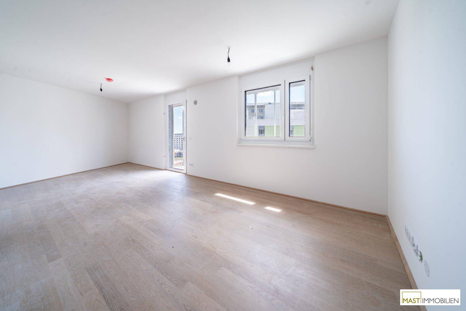 Helles Wohnzimmer mit Zugang zu einem Außenbereich, ausgestattet mit modernem Holzparkett.