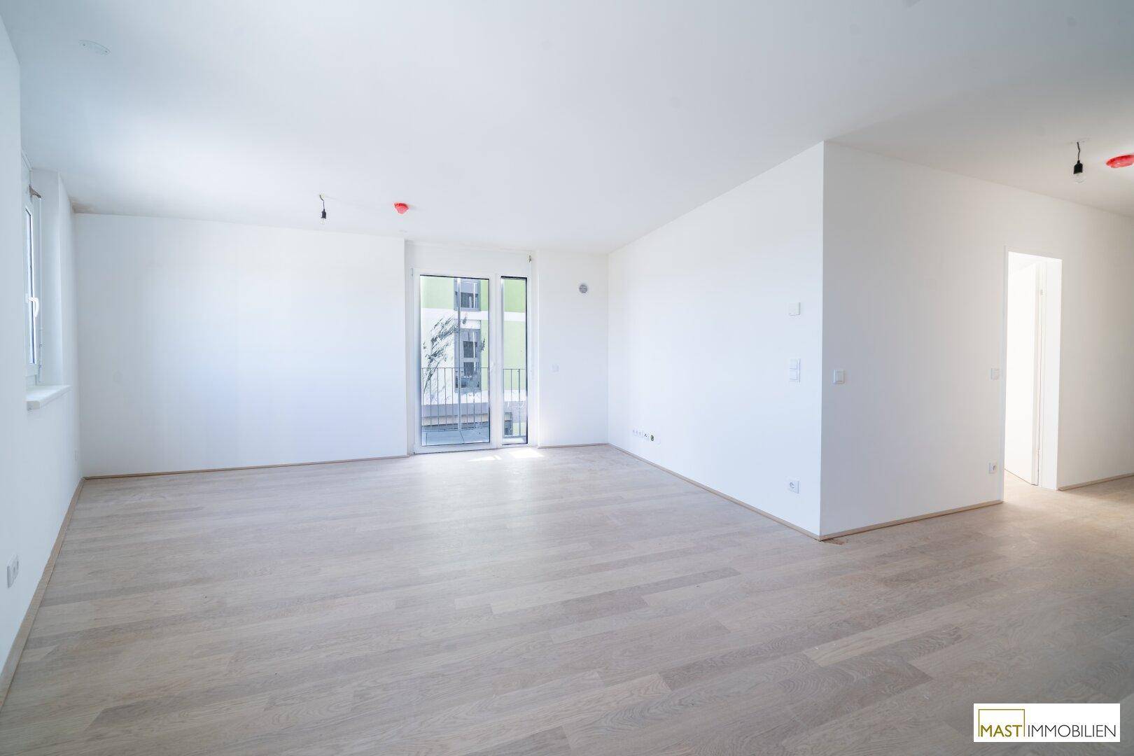 Geräumiges, leeres Wohnzimmer mit hellem Laminatboden und Zugang zu einem französischen Balkon.