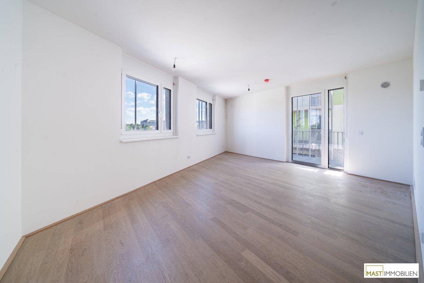 Großzügiges Wohnzimmer mit viel Tageslicht, hellem Laminatboden und Zugang zum französischen Balkon.