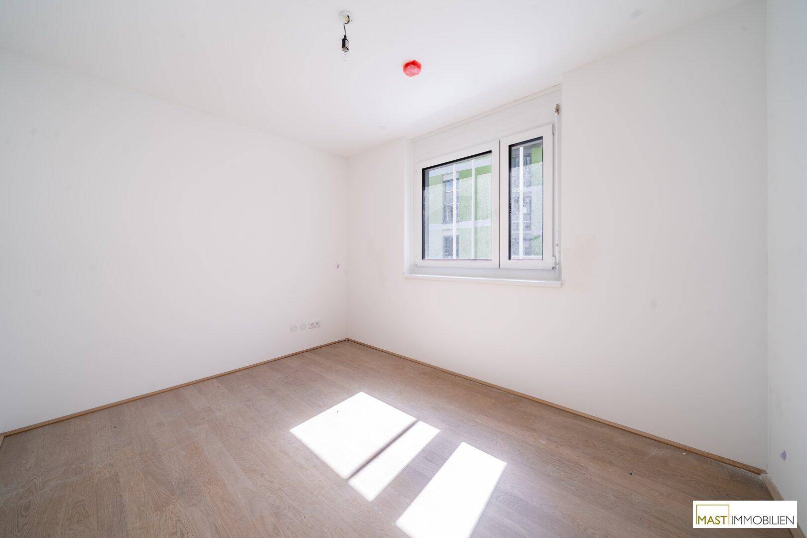Ruhiges Schlafzimmer mit hellem Laminatboden und einem Fenster, das viel Tageslicht hereinlässt.