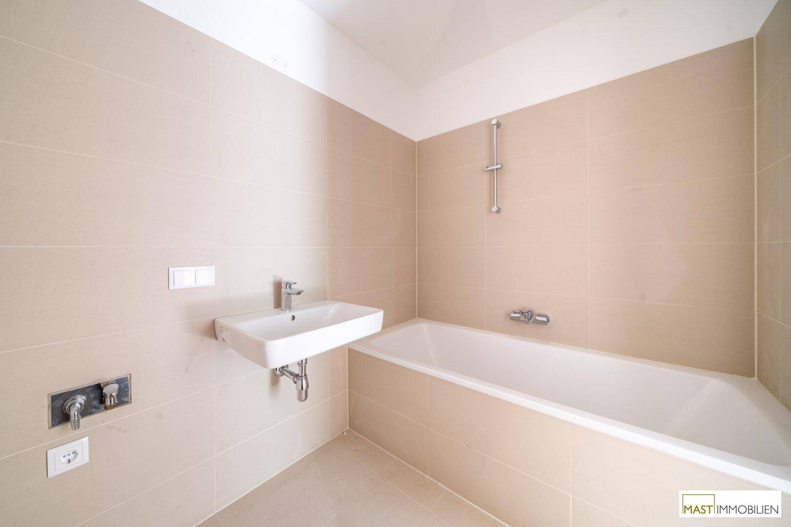 Helles Badezimmer mit Badewanne und modernem Waschbecken, ausgestattet mit beigefarbenen Fliesen.