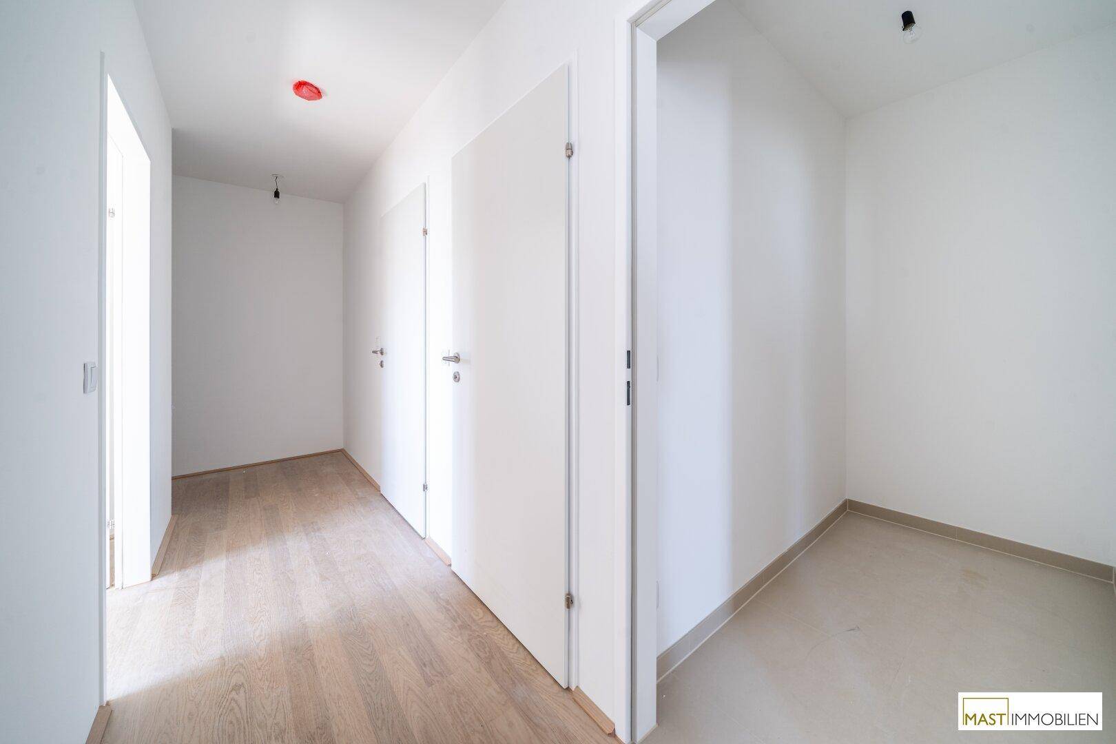 Heller Flur mit verschiedenen Bodenbelägen aus Holz und Fliesen sowie mehreren weißen Türen.