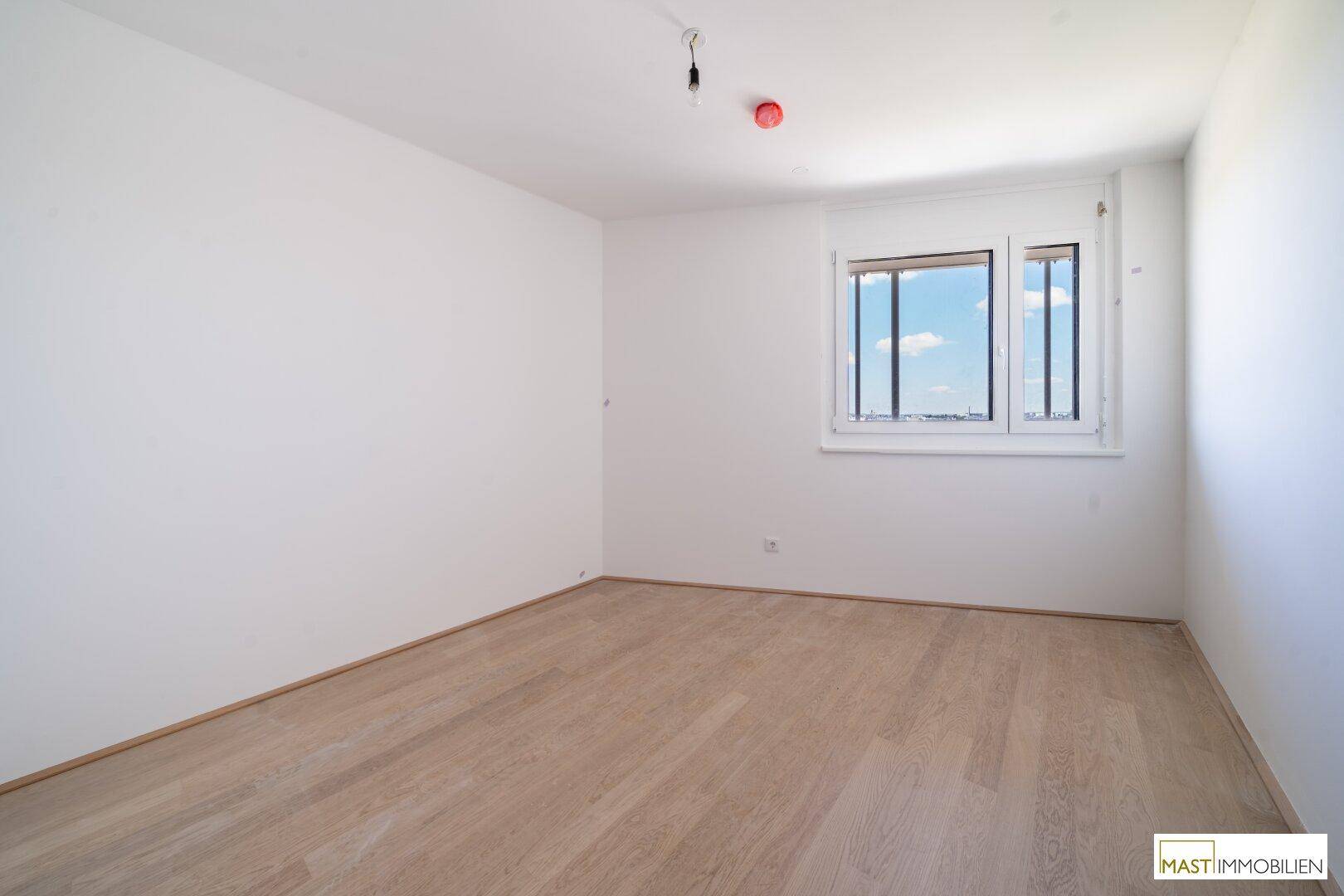 Helles Schlafzimmer mit Holzboden und Fenster, das einen weiten Blick auf die Stadt bietet.