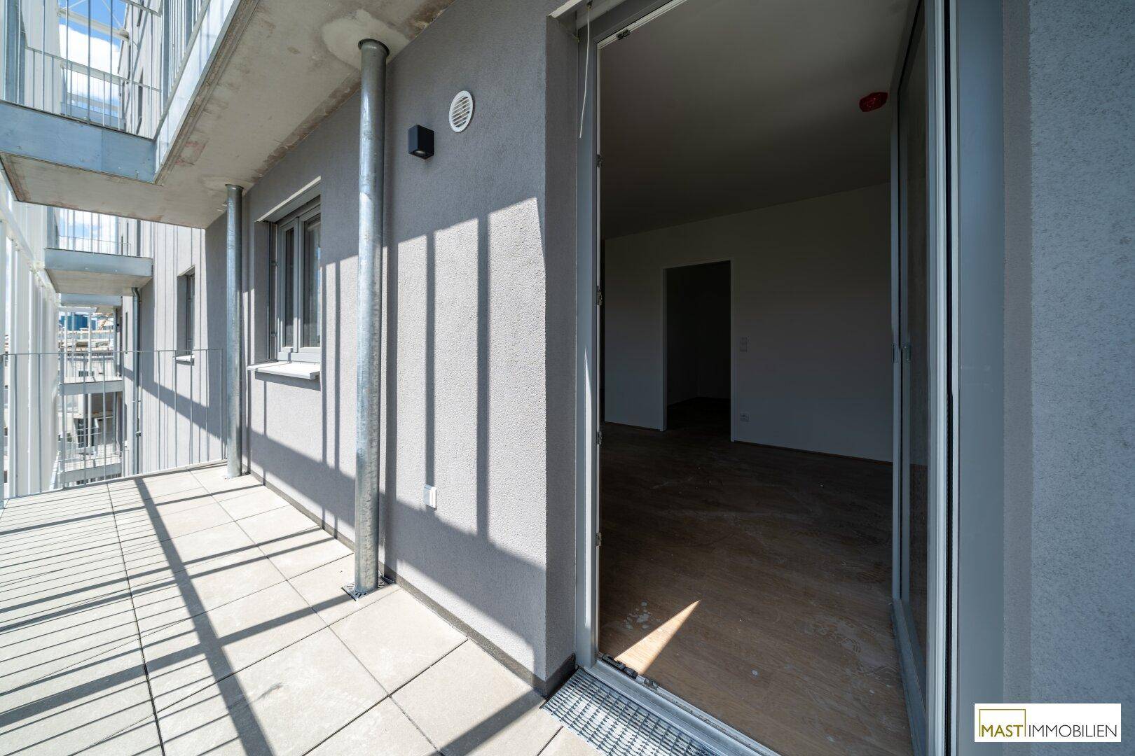 Heller Balkon mit Fliesenboden und modernem Metallgeländer, direkt vom Innenbereich zugänglich.