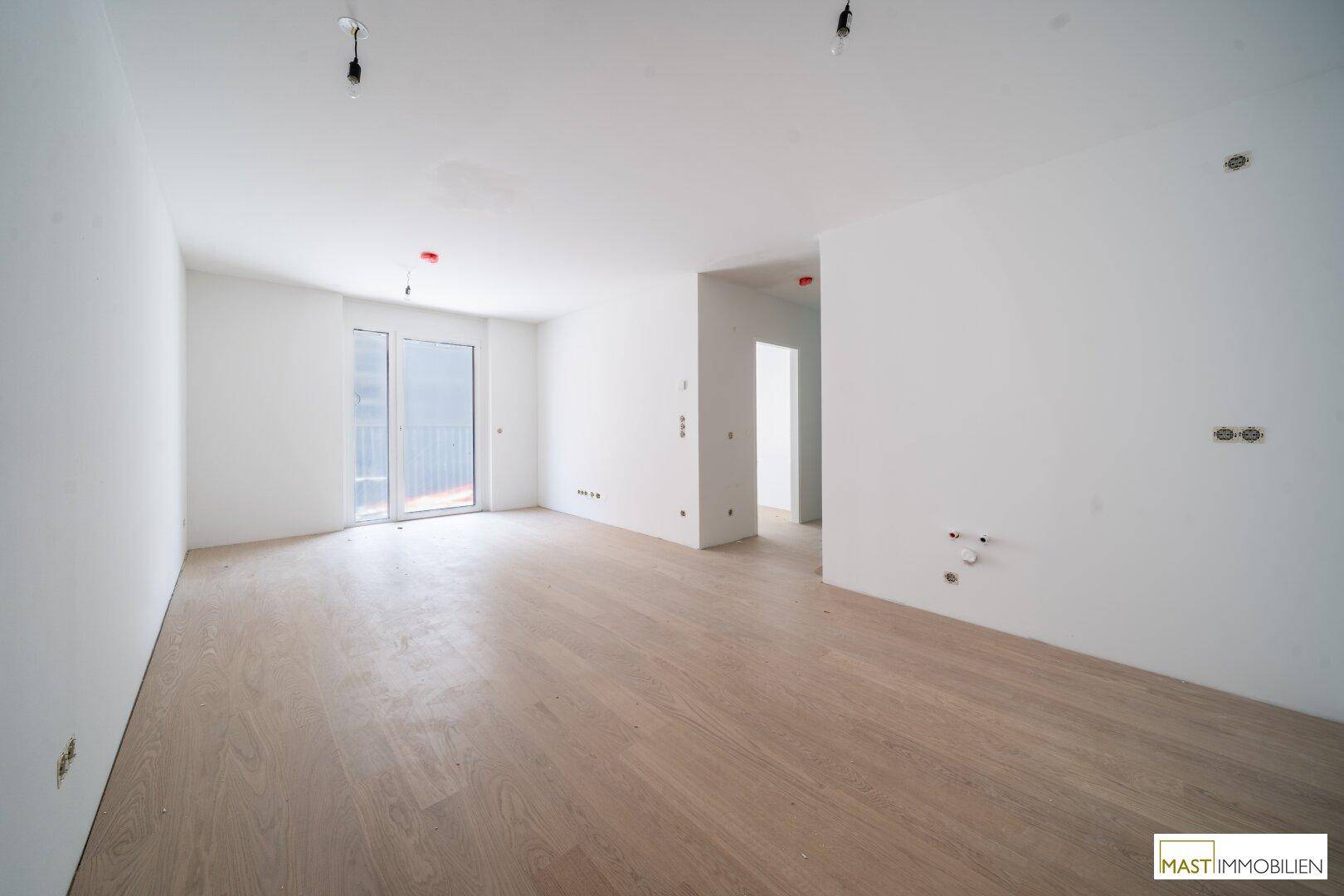 Geräumiger, heller Wohnbereich mit hellem Holzparkett und Zugang zu einem Balkon oder einer Terrasse.