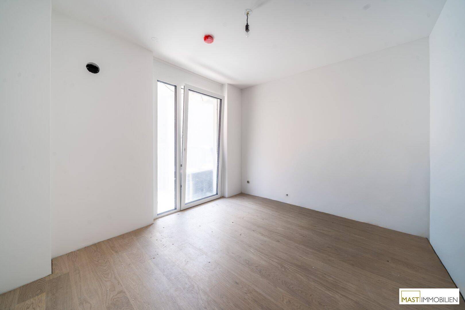 Lichtdurchfluteter Raum mit großen Fenstern und hellem Holzparkett, ideal für ein Schlaf- oder Wohnzimmer.