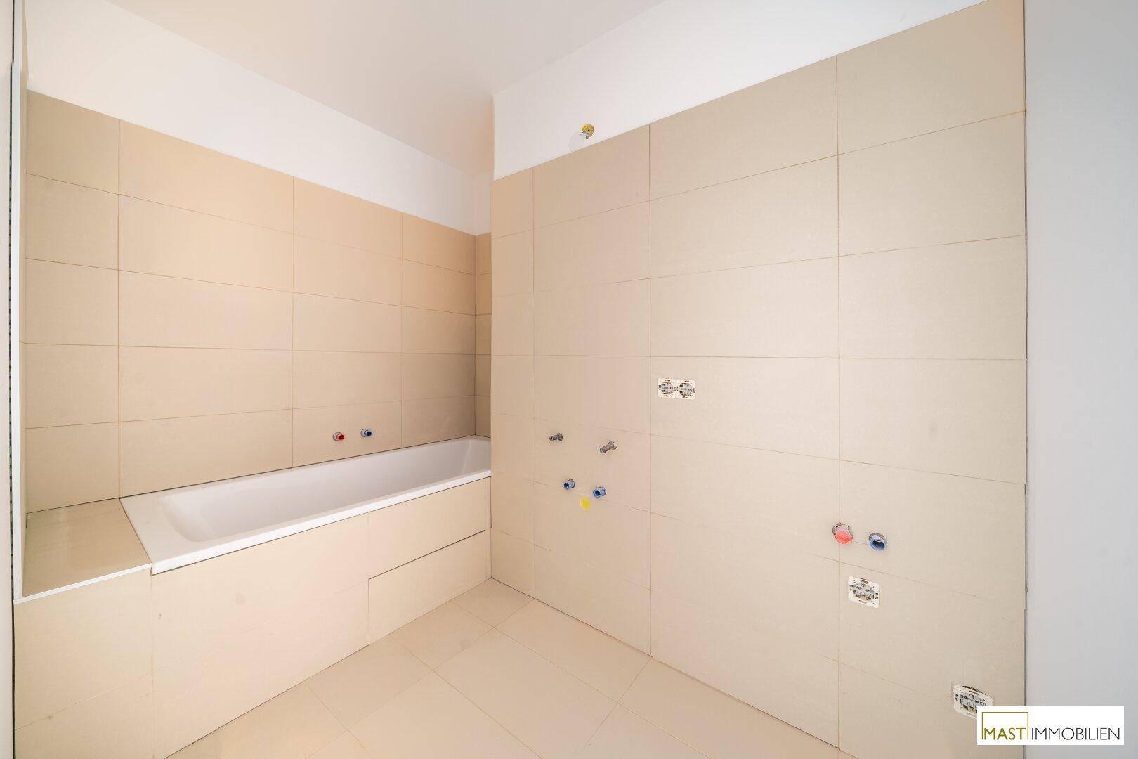 Modernes Badezimmer im Bau mit beigefarbenen Fliesen und einer bereits installierten Badewanne.