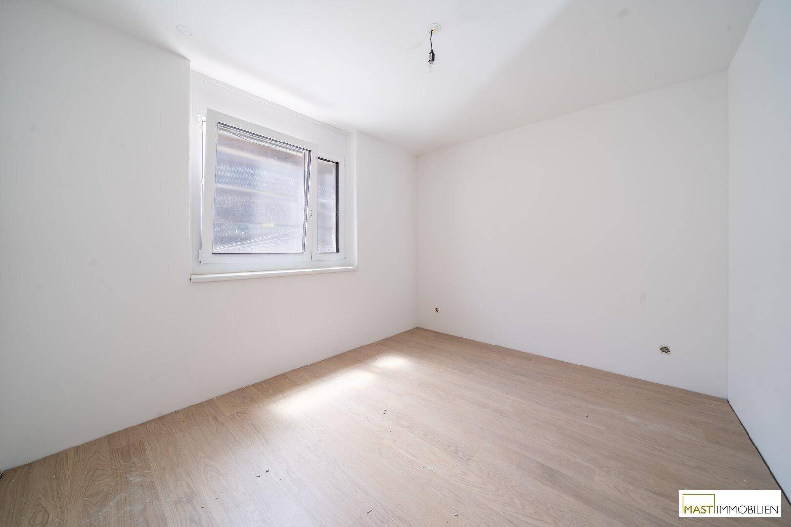Helles Schlafzimmer mit neuem Holzparkett und einem Fenster, das viel Tageslicht hereinlässt.