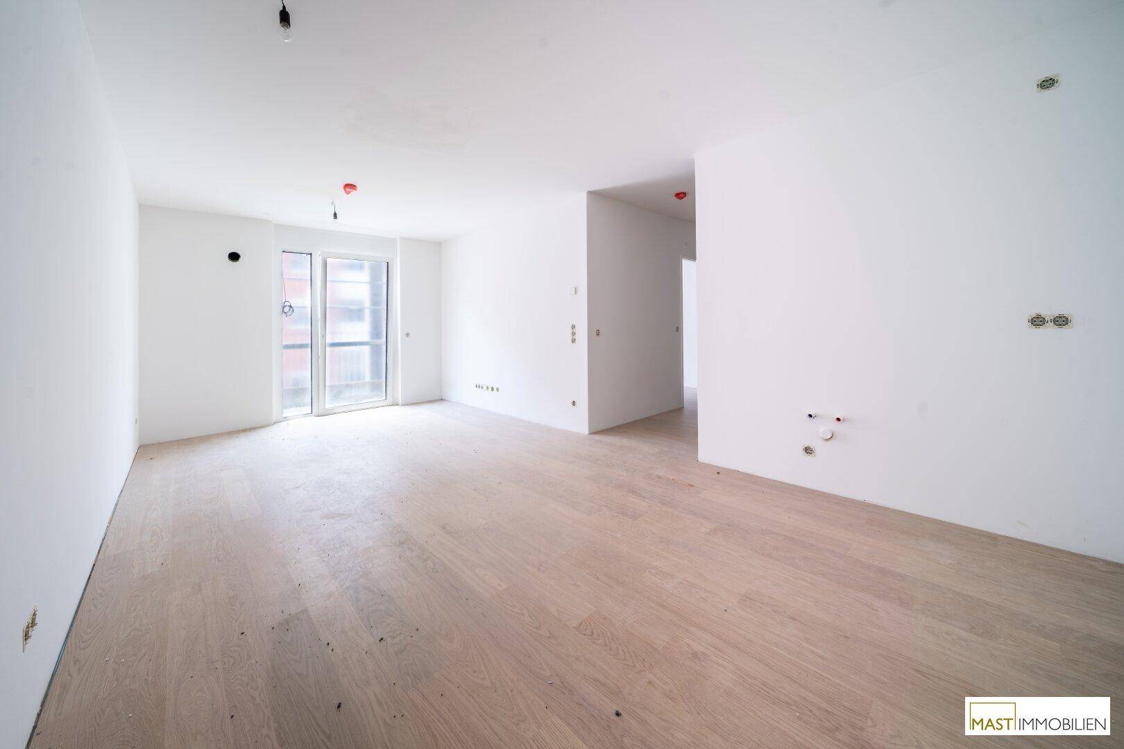 Geräumiges, helles Wohnzimmer mit Holzboden und Zugang zu einem Balkon in einem Neubau.