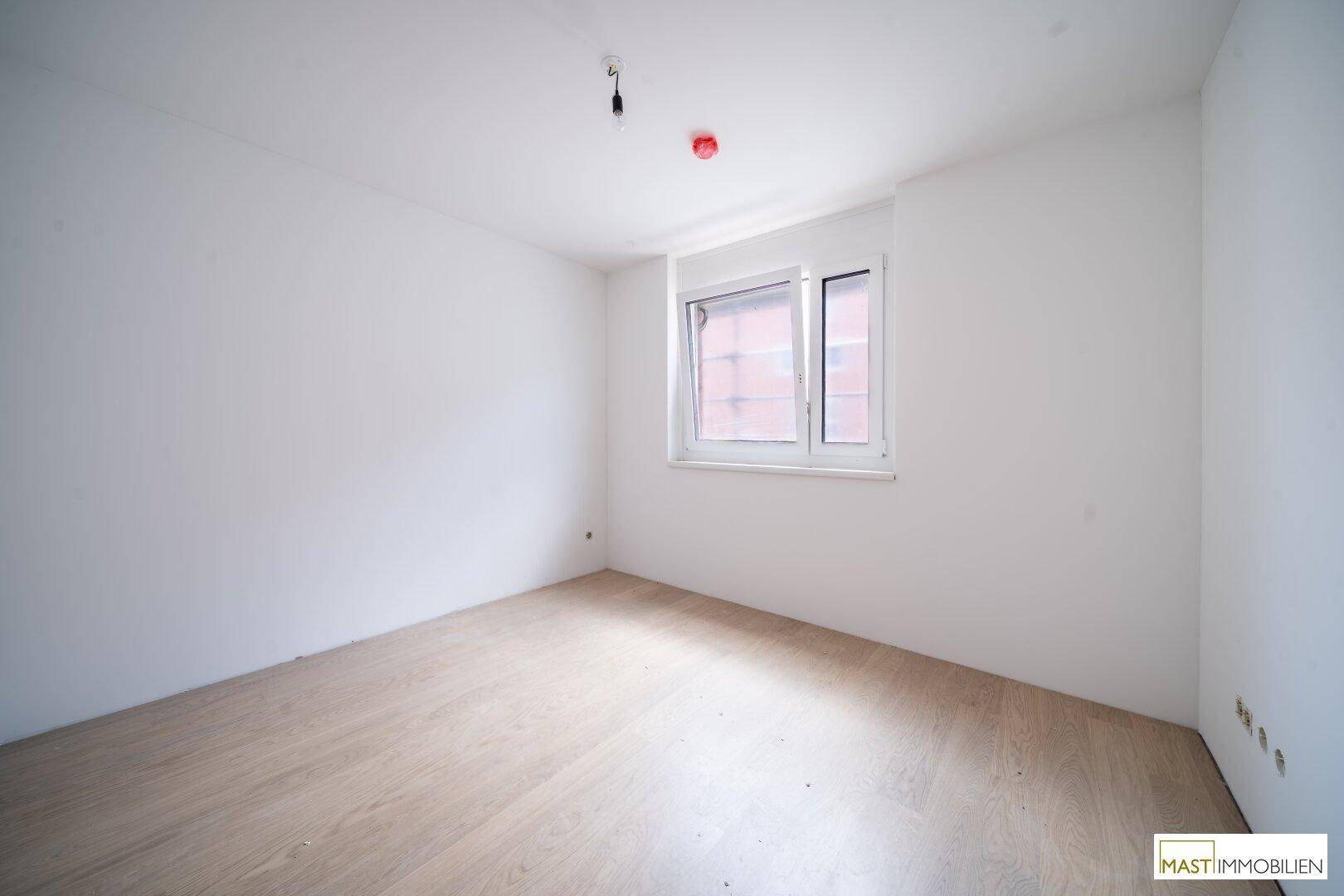Helles Schlafzimmer mit Holzboden und einem Fenster, das viel Tageslicht hereinlässt.
