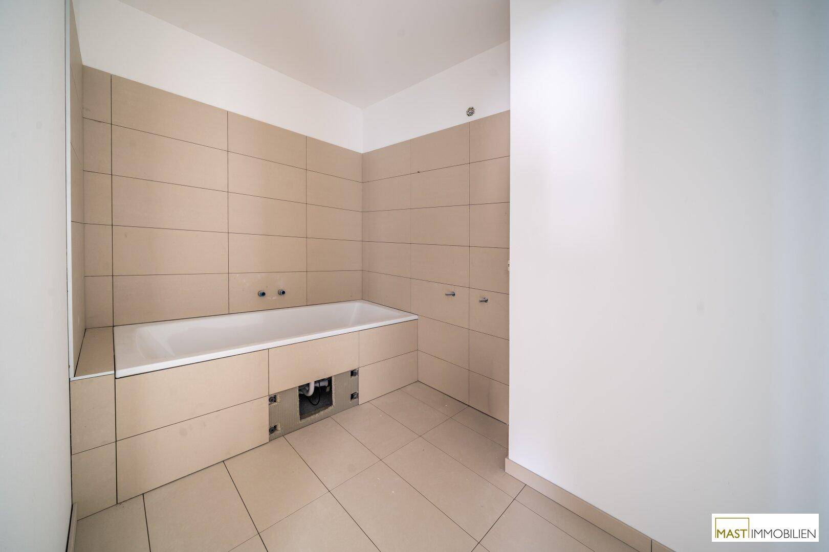 Unfertiges Badezimmer mit eingebauter Badewanne und modernen beigefarbenen Fliesen.