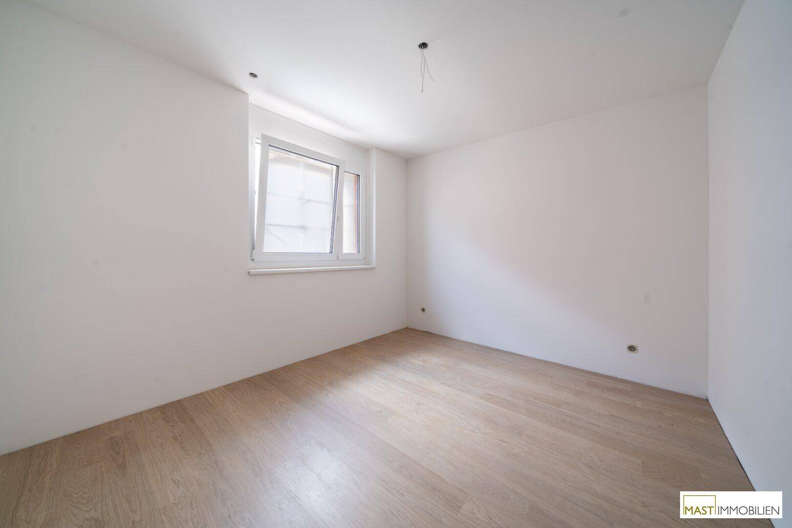 Weiteres helles Schlafzimmer mit Holzboden und einem Fenster für natürliche Belichtung.