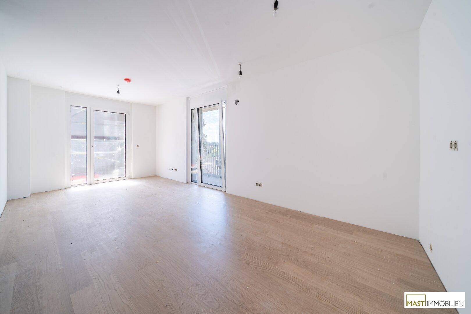 Geräumiges, helles Wohnzimmer mit neuem Laminatboden und zwei großen Zugängen zum Außenbereich.