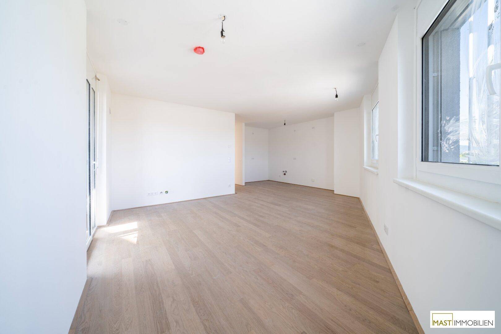 Lichtdurchfluteter Wohnbereich mit großen Fenstern und hellem Laminatboden, bereit zur individuellen Gestaltung.