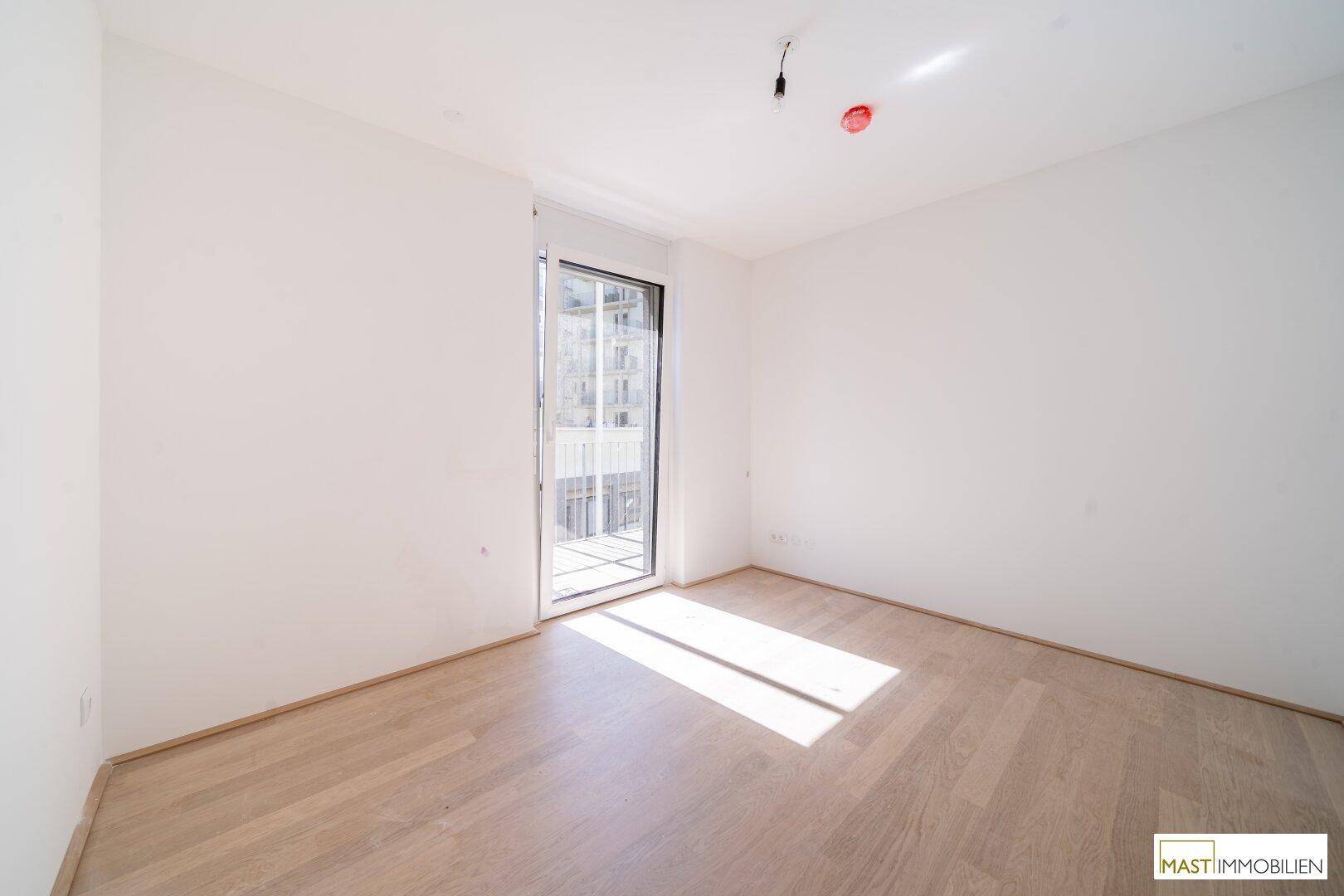 Helles Schlafzimmer mit Laminatboden und direktem Zugang zu einem französischen Balkon.