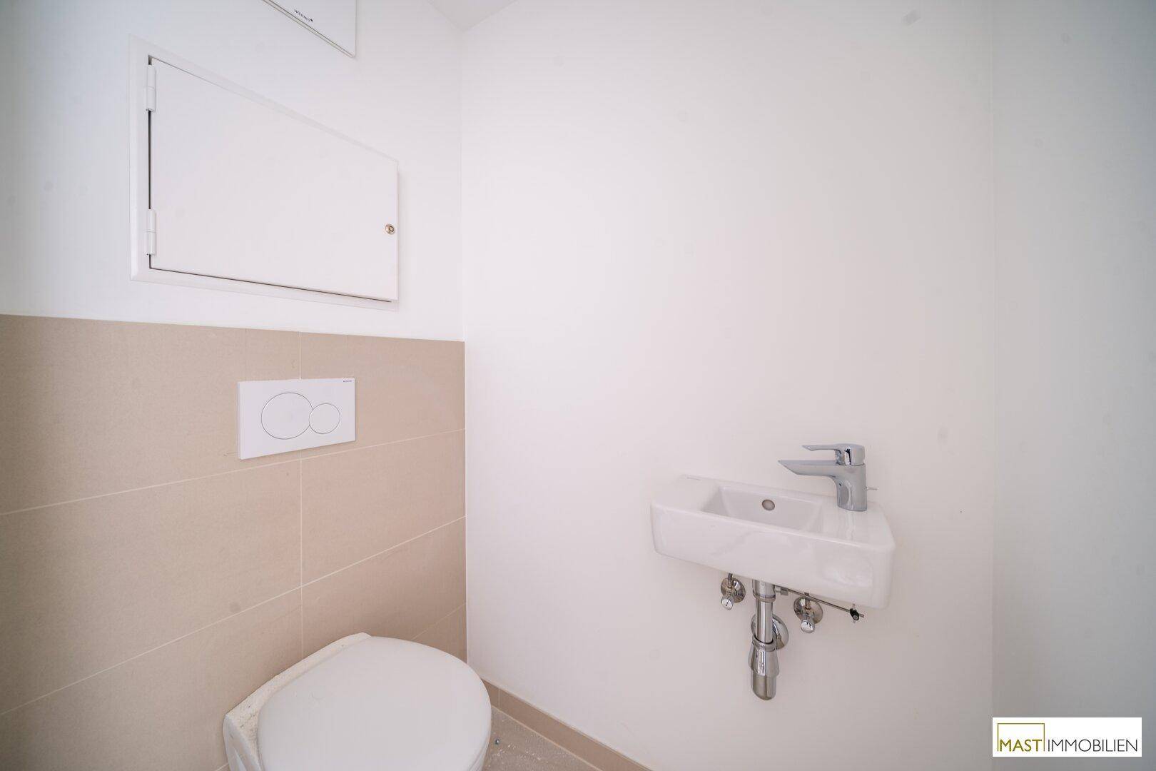 Modernes Gäste-WC mit wandhängendem WC und kleinem Waschbecken, hell gefliest.