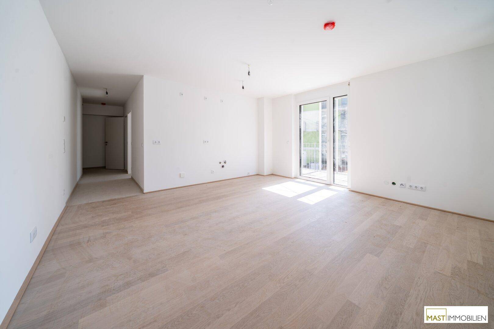 Weitläufiger Wohnbereich mit hellem Holzboden und viel Tageslicht durch die großen Fenster.