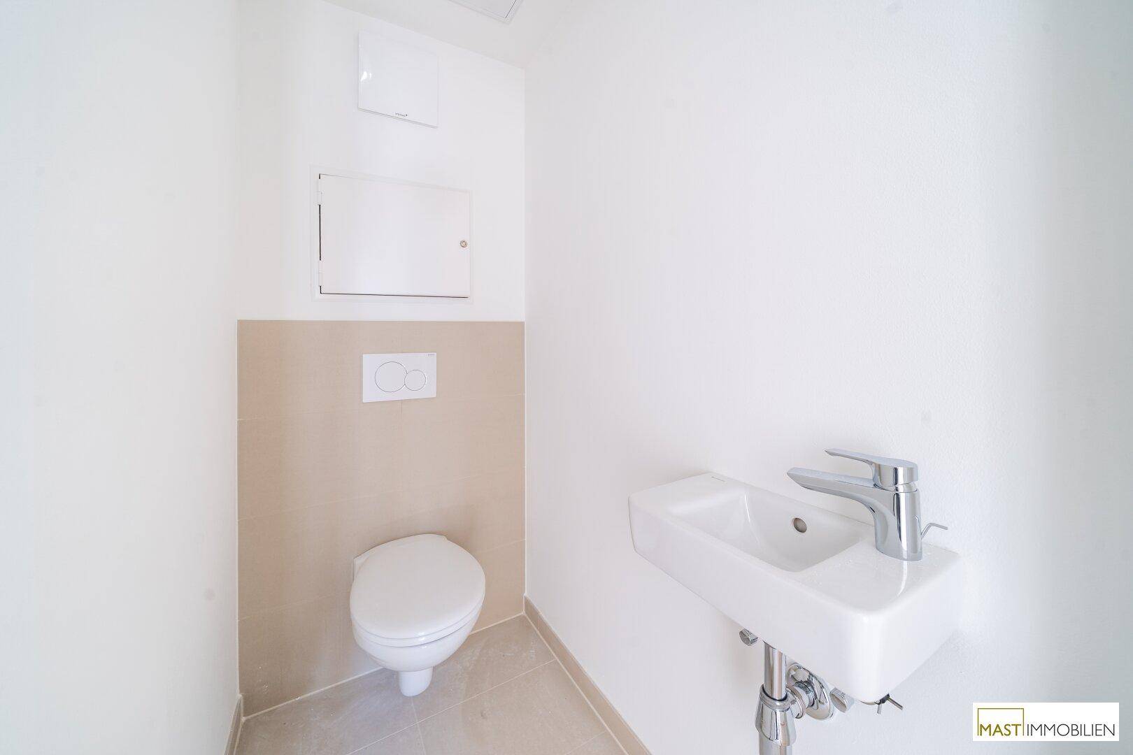 Modernes Gäste-WC mit wandhängender Toilette, kleinem Waschbecken und beigefarbenen Wandfliesen.