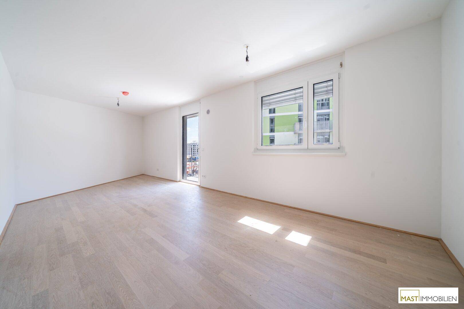 Heller Wohnraum mit Zugang zu einem Balkon und einem großen Fenster, das viel Licht hereinlässt.