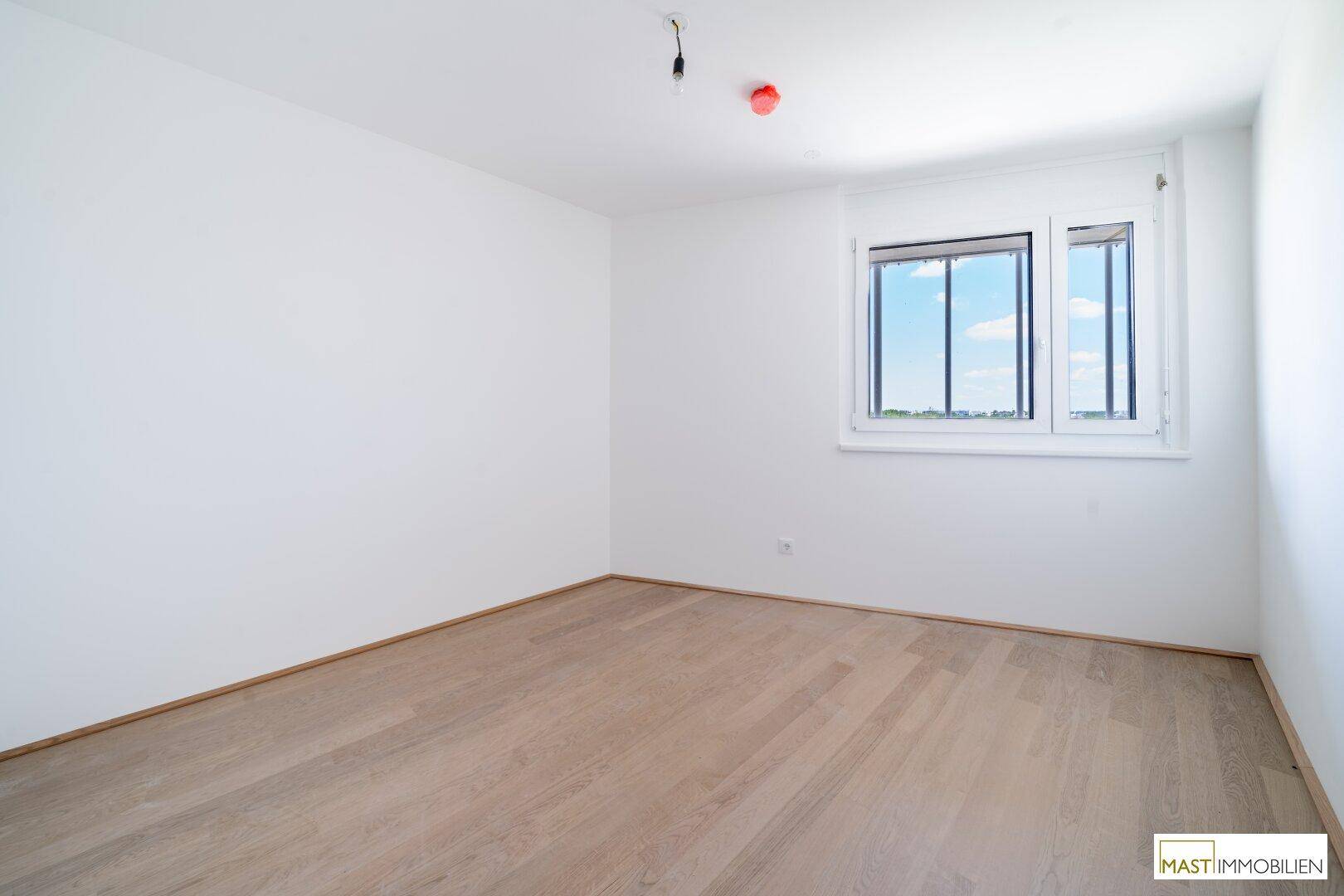 Ruhiges Schlafzimmer mit weiß gestrichenen Wänden, hellem Holzfußboden und Blick auf den blauen Himmel.