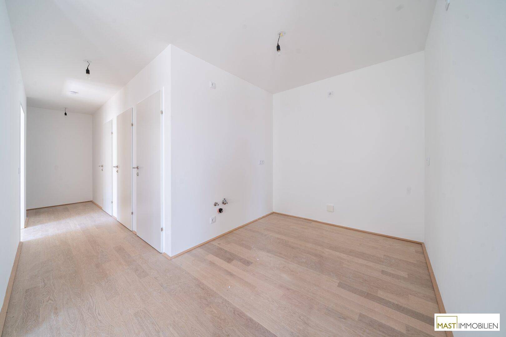 Heller Raum, vorbereitet für eine Küche, mit sichtbaren Anschlüssen und hellem Holzfußboden.