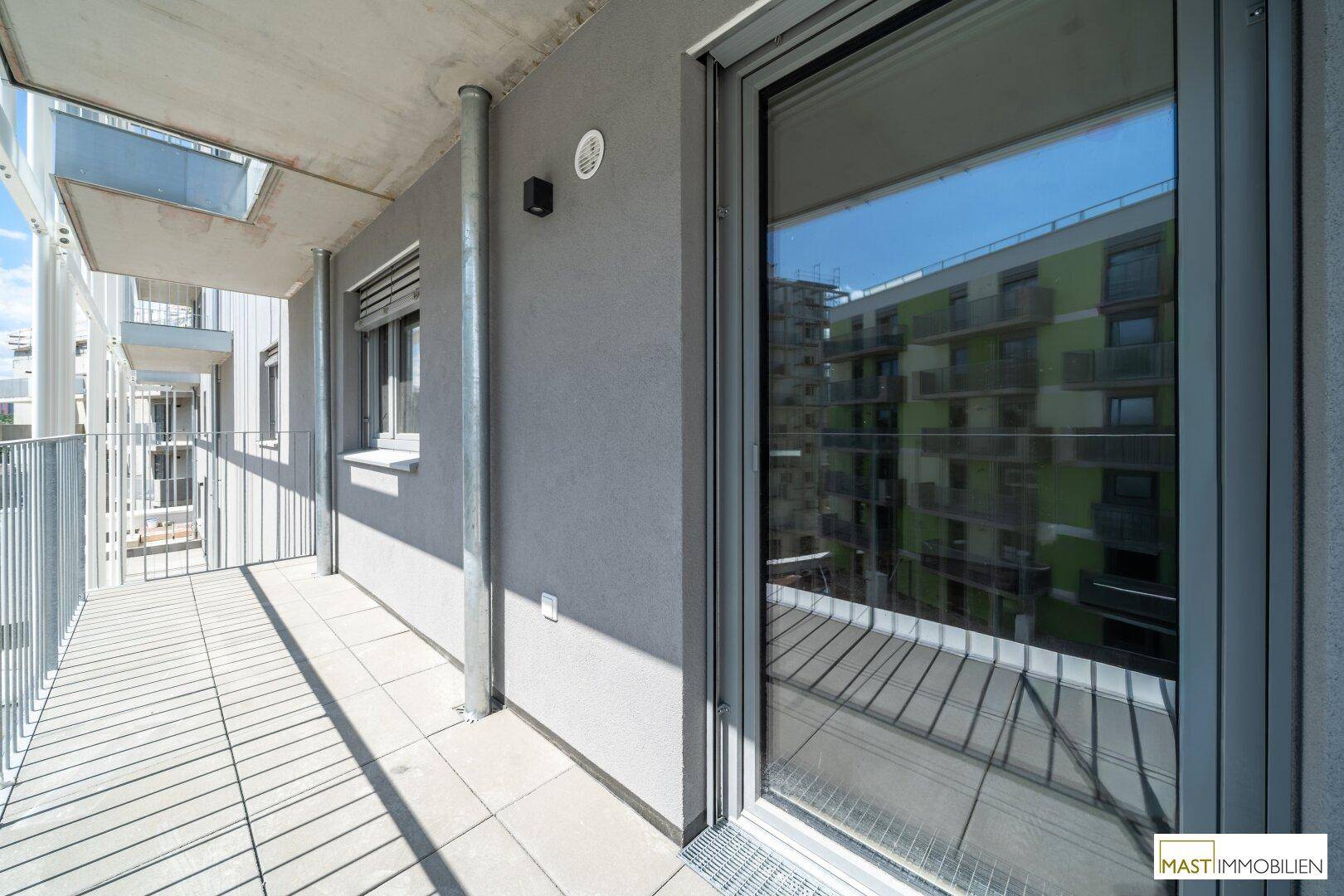 Geräumiger Balkon mit Fliesenboden und Metallgeländer, bietet einen Blick auf die umliegenden Gebäude.