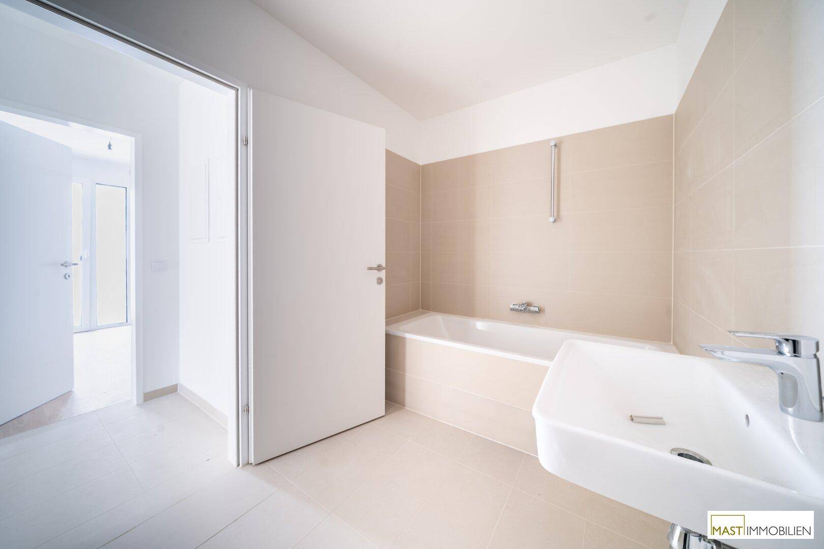 Modernes Badezimmer mit Badewanne, Einzelwaschbecken und hellen Fliesen, bereit zur Nutzung.