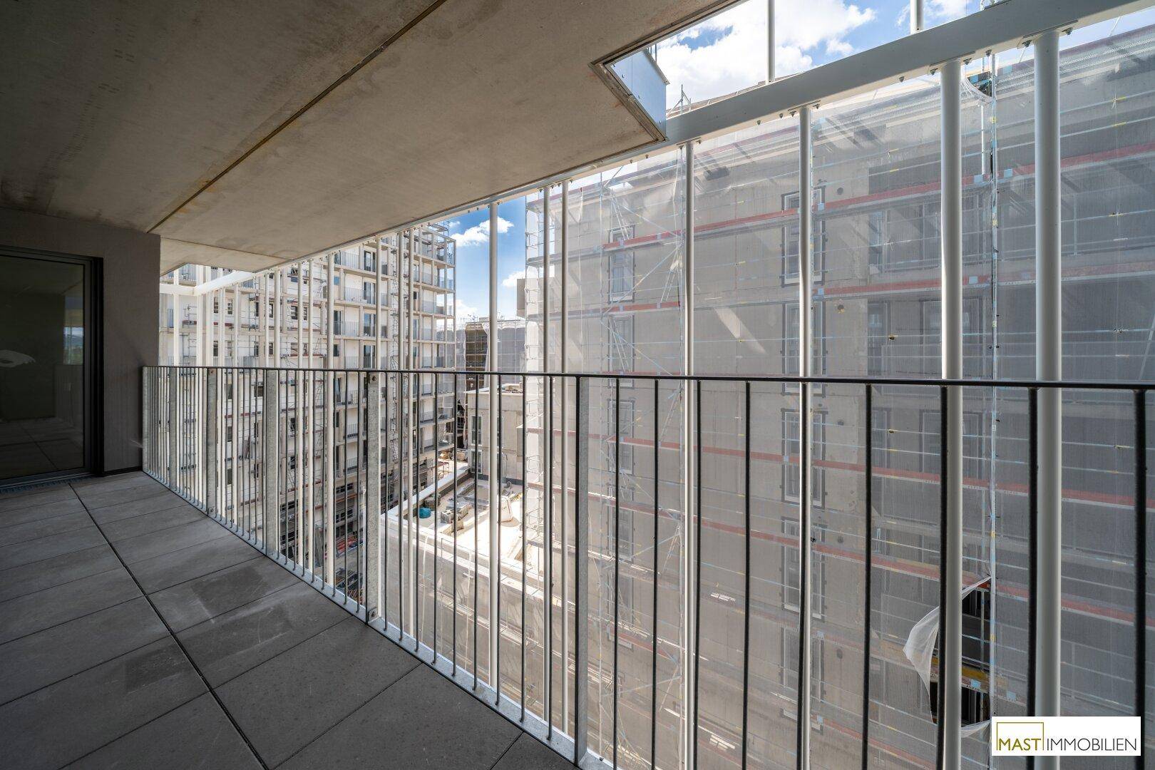 Geräumiger Balkon mit Fliesenboden und Metallgeländer, bietet Blick auf die umliegenden Gebäude.