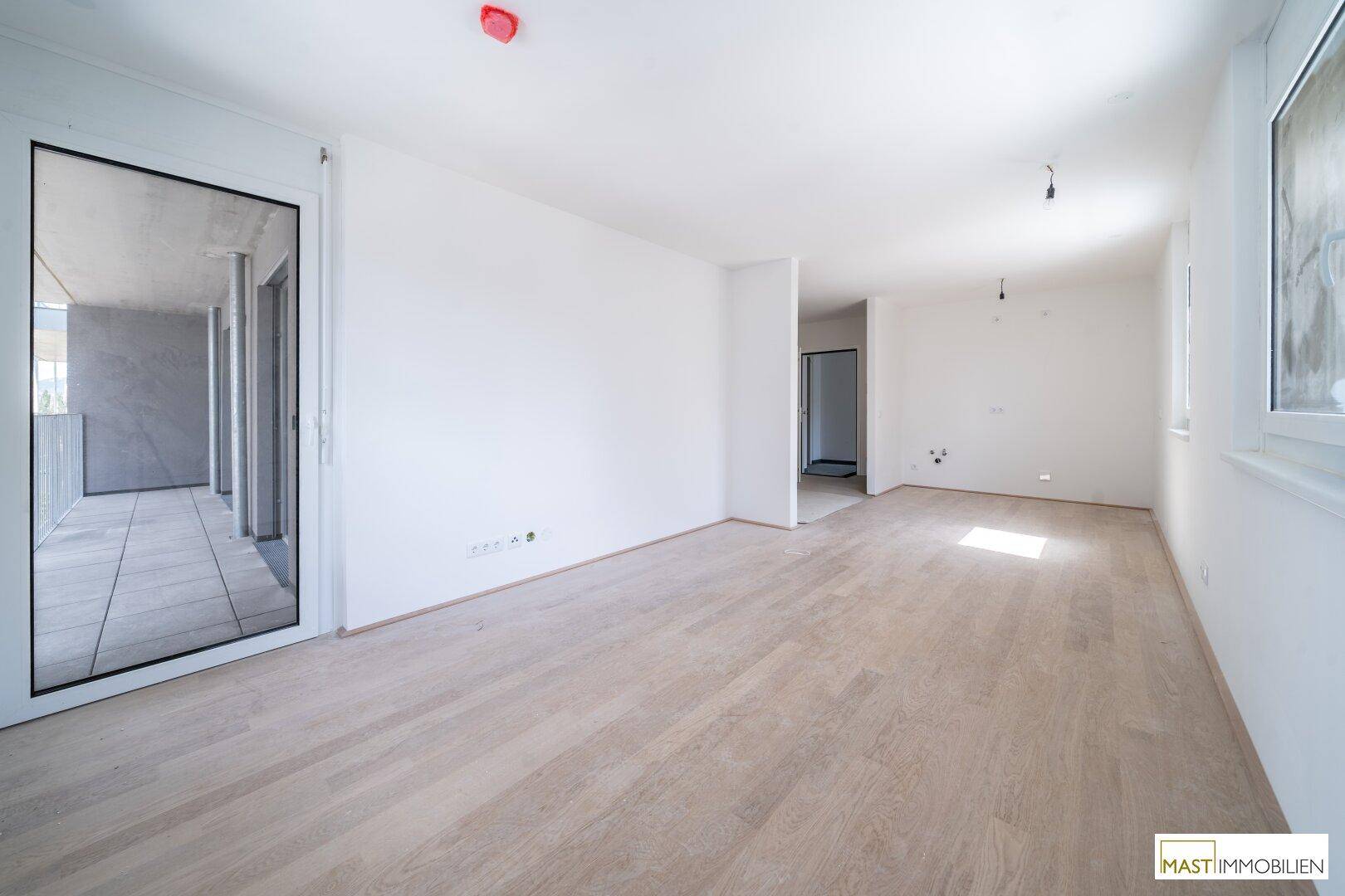 Heller Wohnbereich mit Holzboden und großem Balkonzugang, bietet offene Gestaltungsmöglichkeiten.