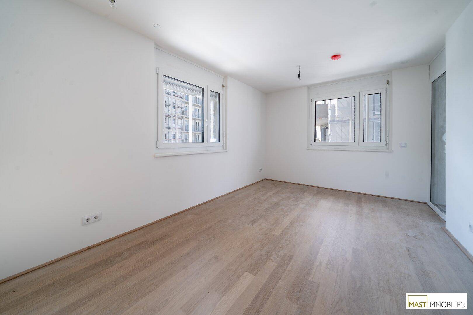 Freundliches Zimmer mit hellem Holzboden und zwei Fenstern, ideal als Schlaf- oder Arbeitszimmer.