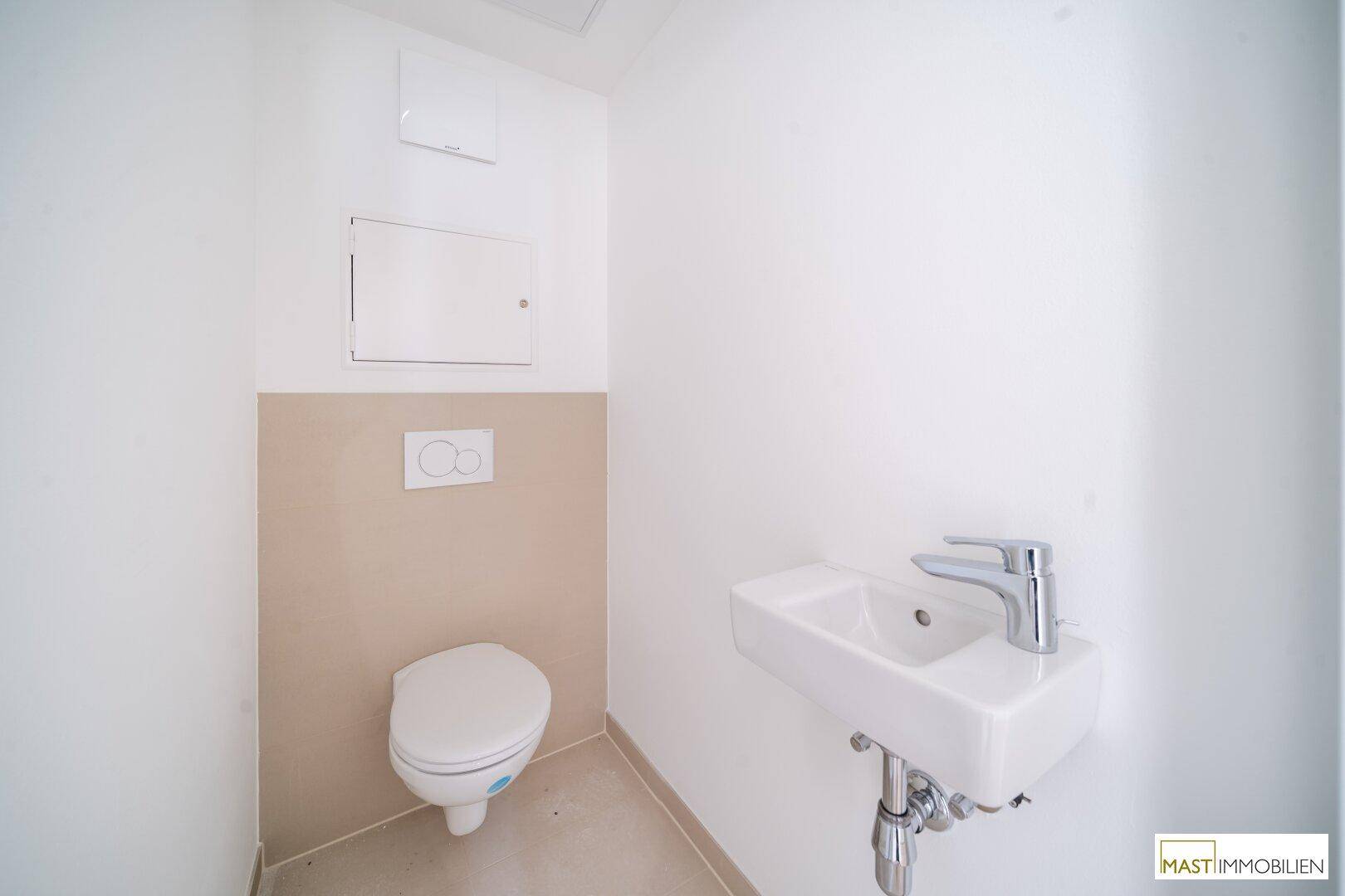 Modernes Gäste-WC mit wandhängender Toilette und kleinem Waschbecken in neutralen Farbtönen.