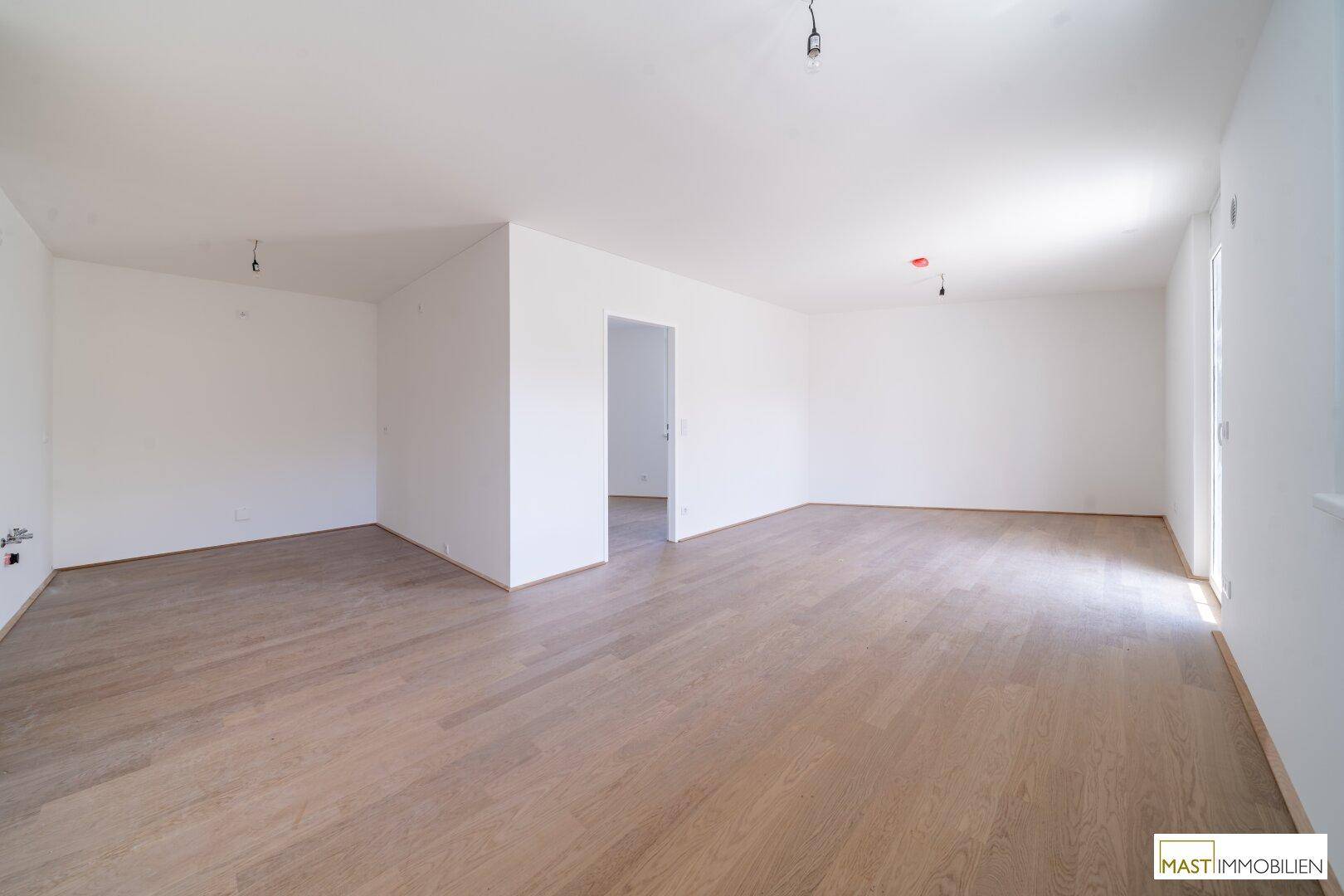 Geräumiges, leeres Wohnzimmer mit hellem Holzboden und weißen Wänden, bereit zur individuellen Gestaltung.
