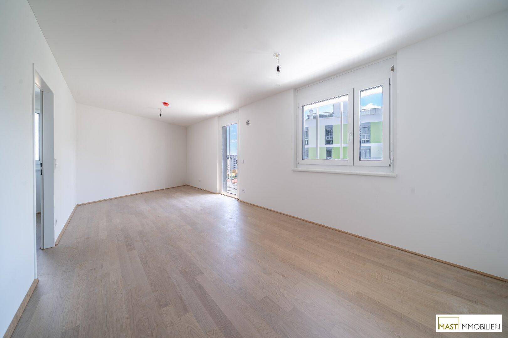 Helles, leeres Zimmer mit Parkettboden und Zugang zu einem Balkon, ideal als Wohnbereich.