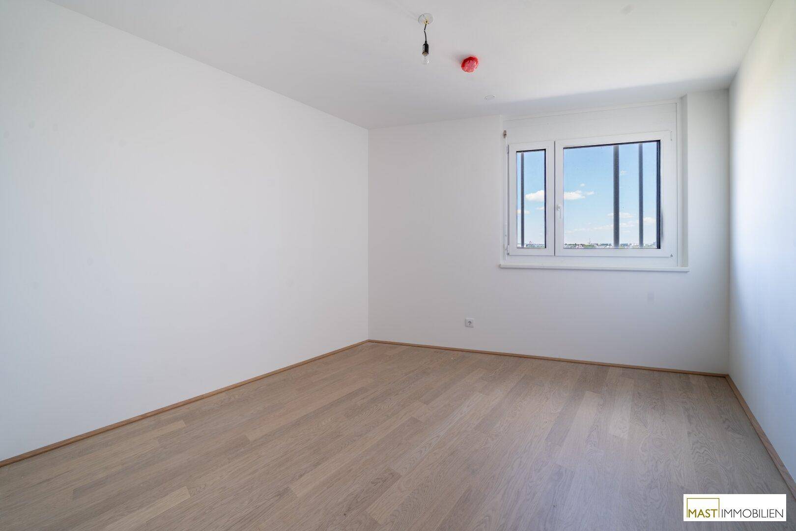 Helles Schlafzimmer mit Parkettboden und Fenster, das einen weiten Blick in die Ferne bietet.
