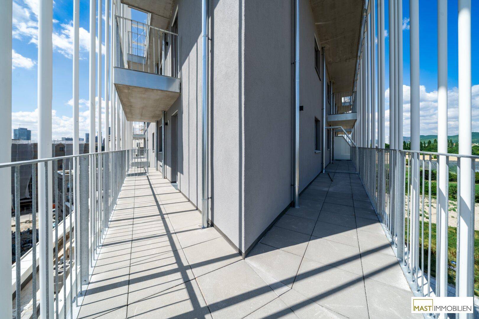 Langer Balkon mit Fliesenboden und modernen Metallgeländern, der sich entlang der Fassade erstreckt.
