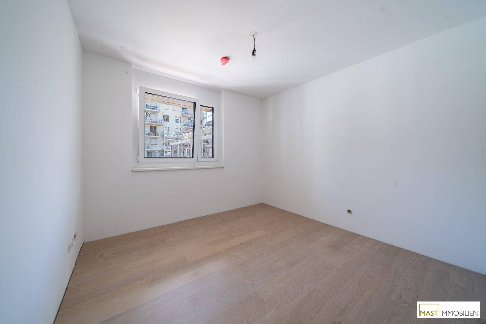 Helles Schlafzimmer mit Holzboden und Fenster, das viel Tageslicht hereinlässt.
