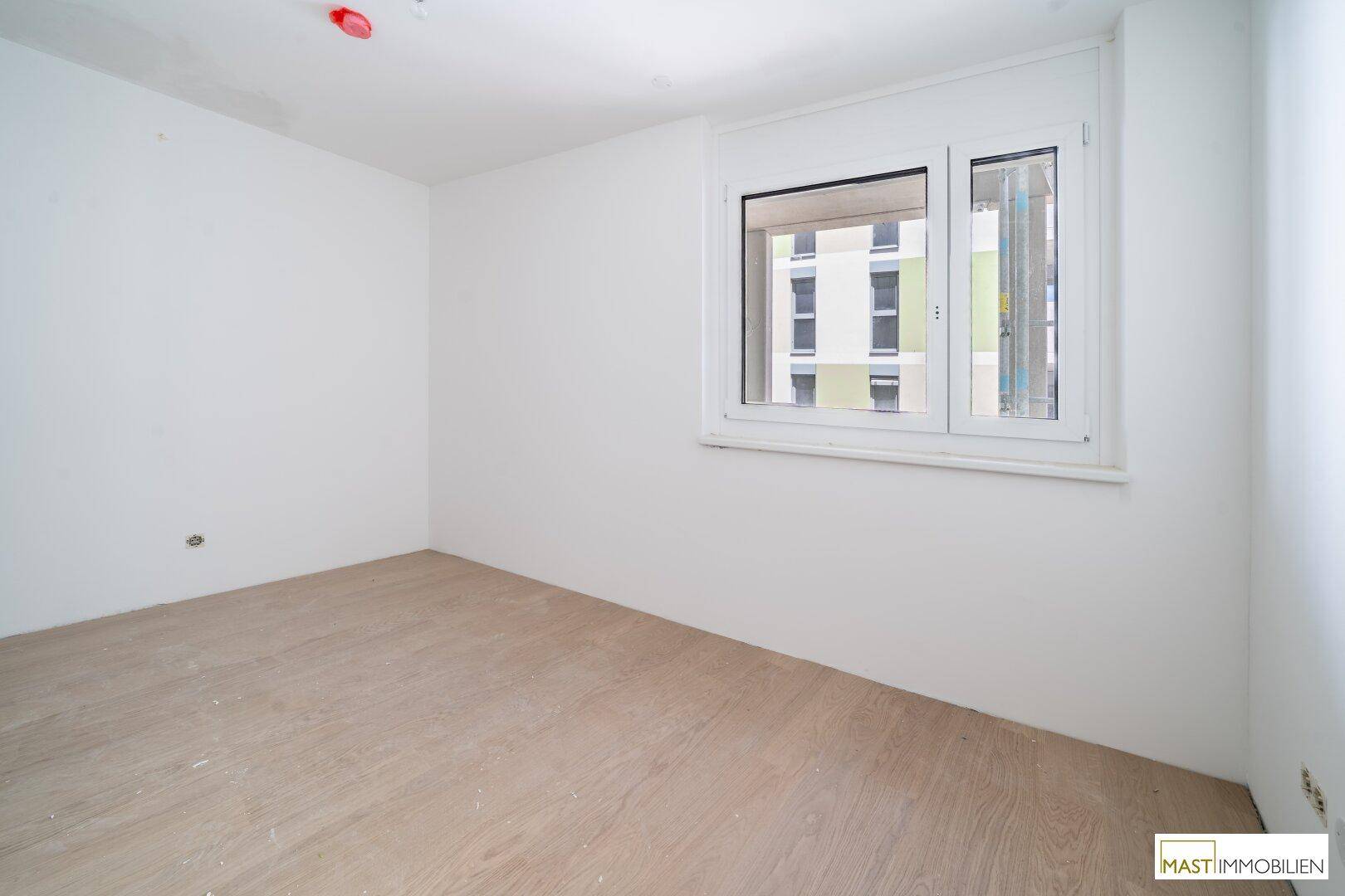 Helles Schlafzimmer mit Holzboden und großem Fenster, das einen Blick nach draußen bietet.