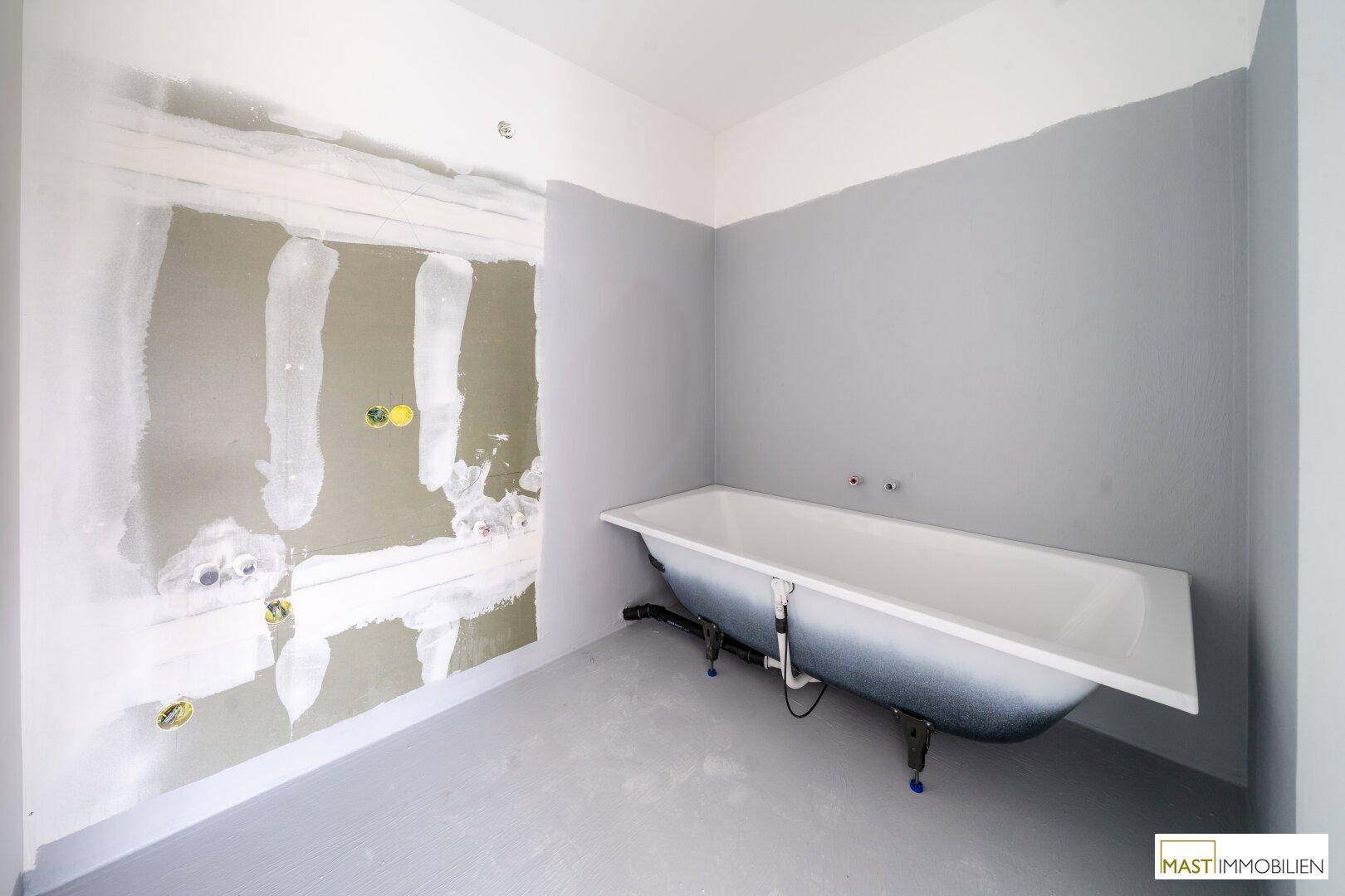 Badezimmer im Rohbau mit einer freistehenden Badewanne und grauen Wänden.
