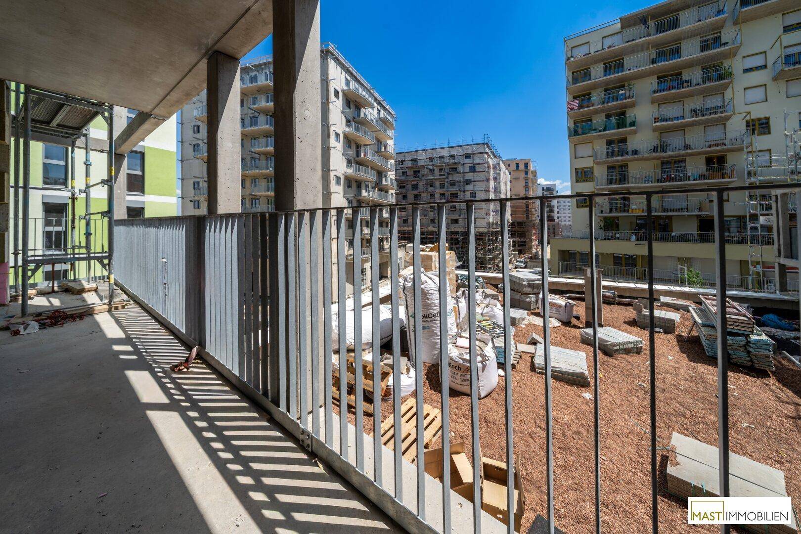 Balkon im Bau mit Metallgeländer und Blick auf umliegende Gebäude und Baustellen.