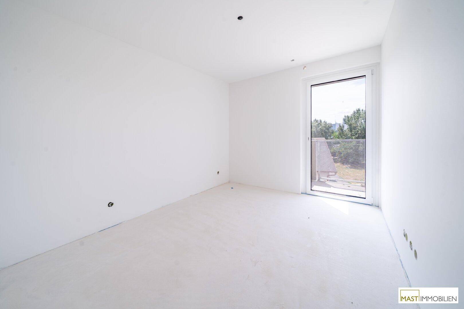 Helles Schlafzimmer im Rohbau mit Zugang zu einem Balkon und Blick ins Grüne.
