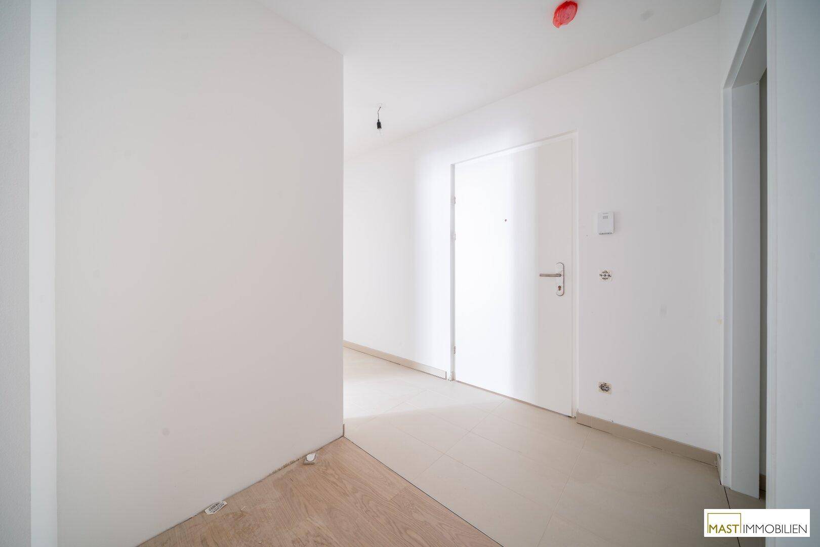 Eingangsbereich mit heller Tür und zwei verschiedenen Bodenbelägen in einem Neubau.