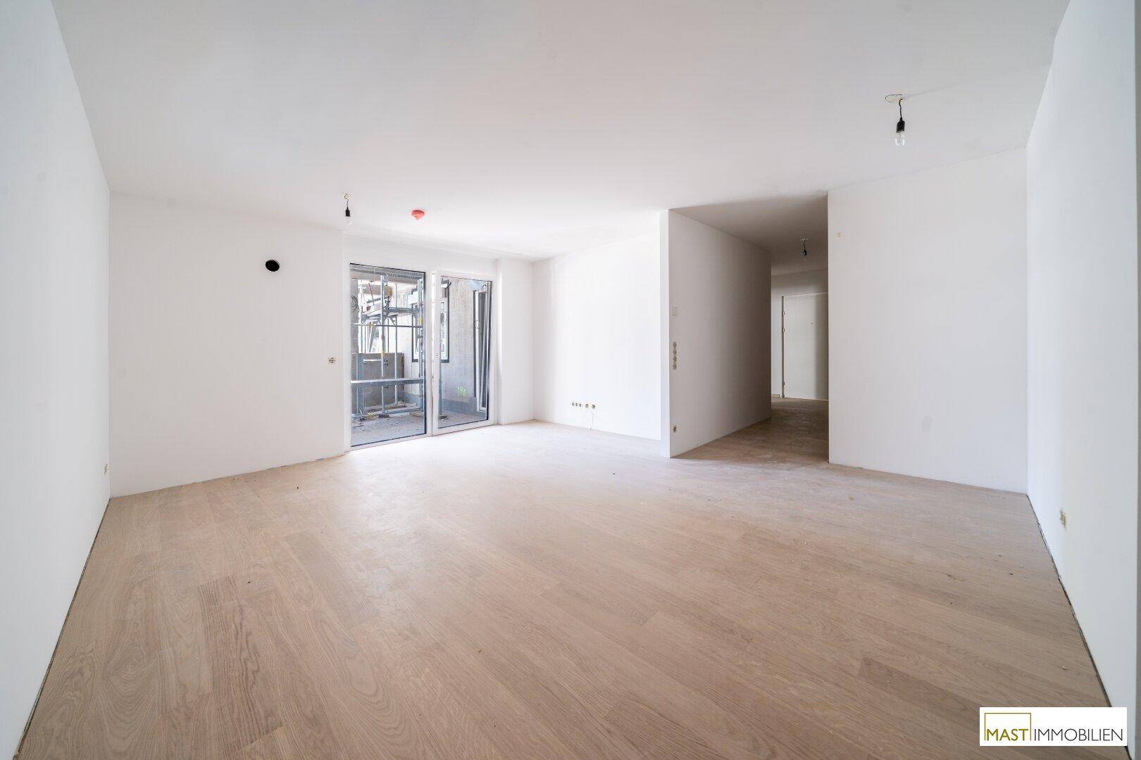 Geräumiges Wohnzimmer mit hellem Laminatboden und großem Zugang zum Balkon.