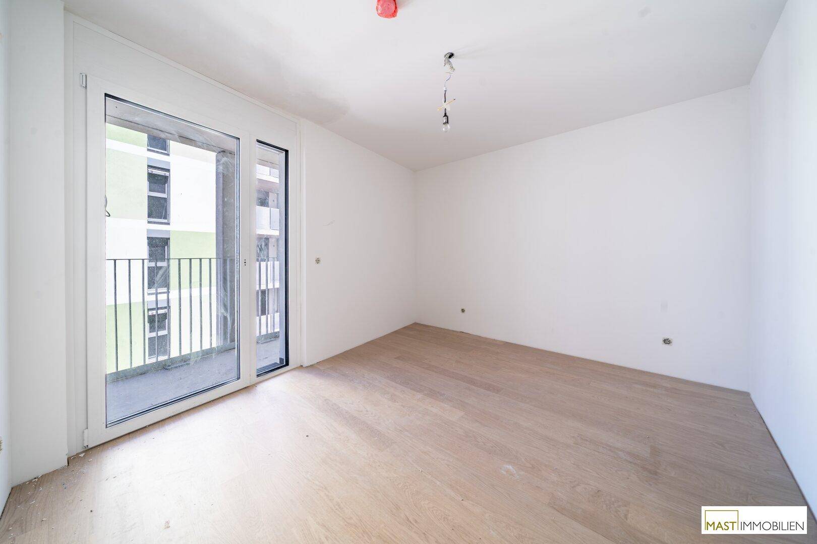 Helles Zimmer mit Holzboden und Zugang zu einem Balkon, ideal als Schlaf- oder Wohnbereich.