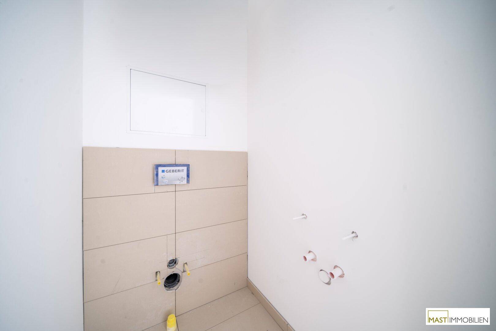 Badezimmer im Bau mit vorbereiteter Wandtoilette und Fliesenboden, bereit für die Endmontage.
