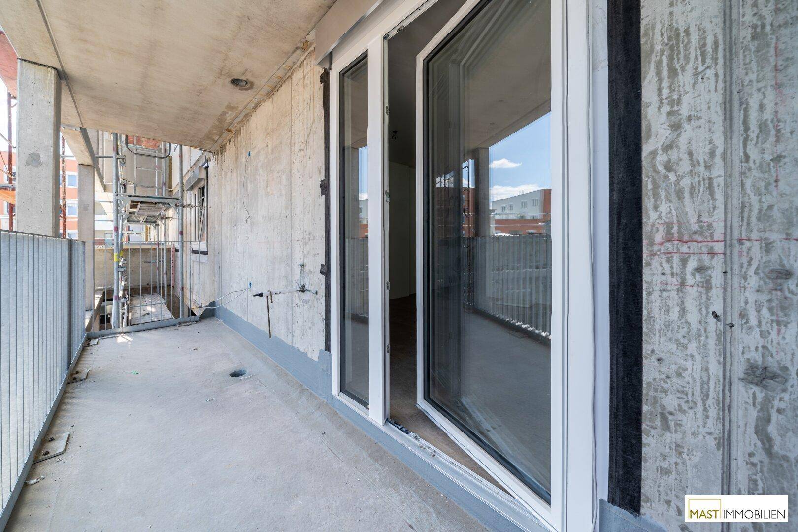 Unmöblierter Balkon mit Betonboden und Metallgeländer, umgeben von Neubauten und Baustellen.