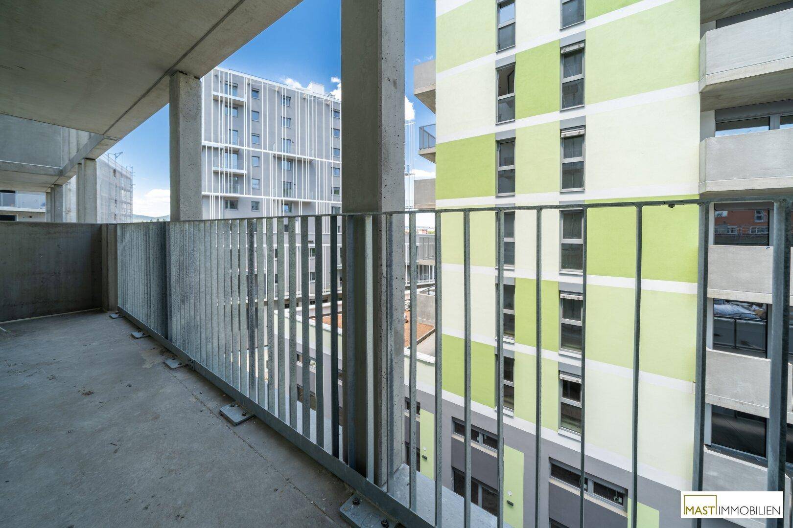 Balkon mit Blick auf moderne Gebäude, darunter eines mit auffälliger grün-weißer Fassadengestaltung.