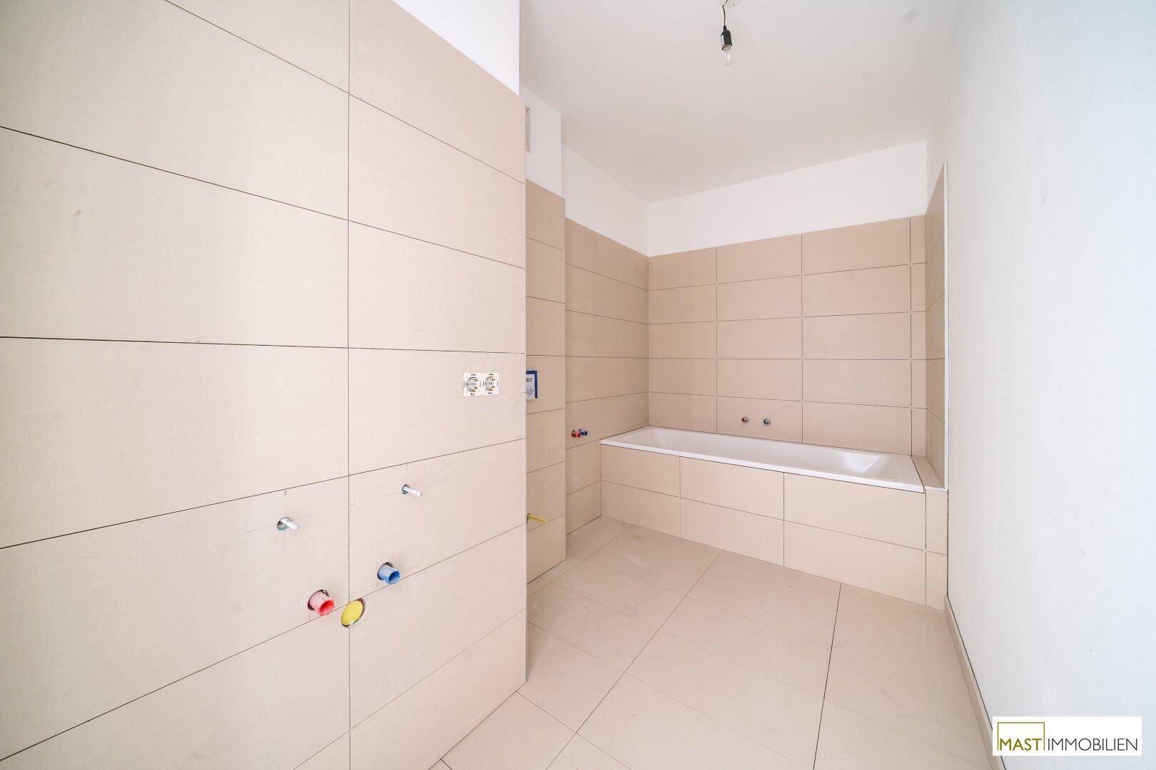 Badezimmer im Bau mit eingebauter Badewanne und Fliesen an Wänden und Boden.