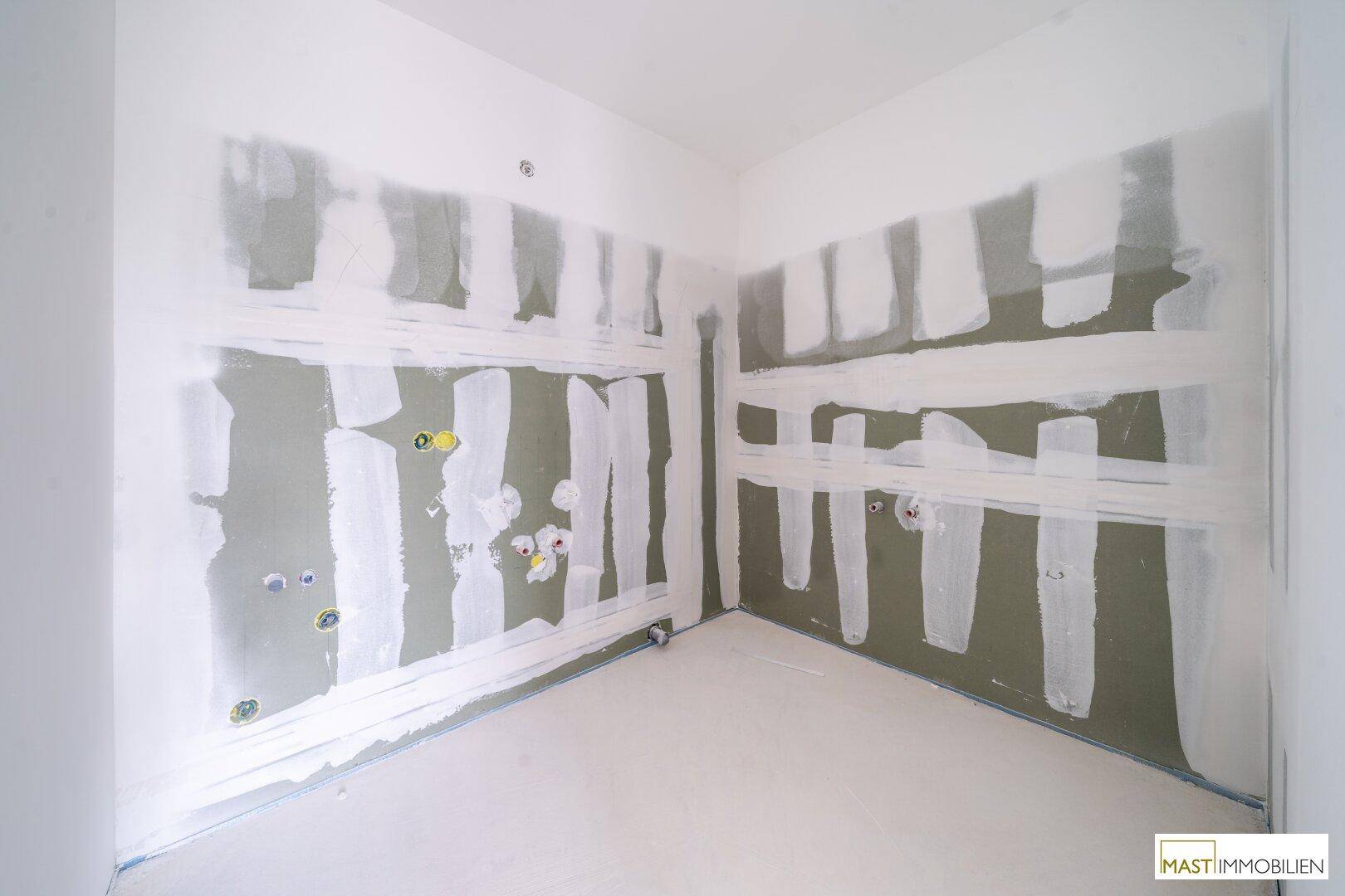 Badezimmer im Rohbau mit vorbereiteten Wänden für Fliesen und sichtbaren Sanitärinstallationen.