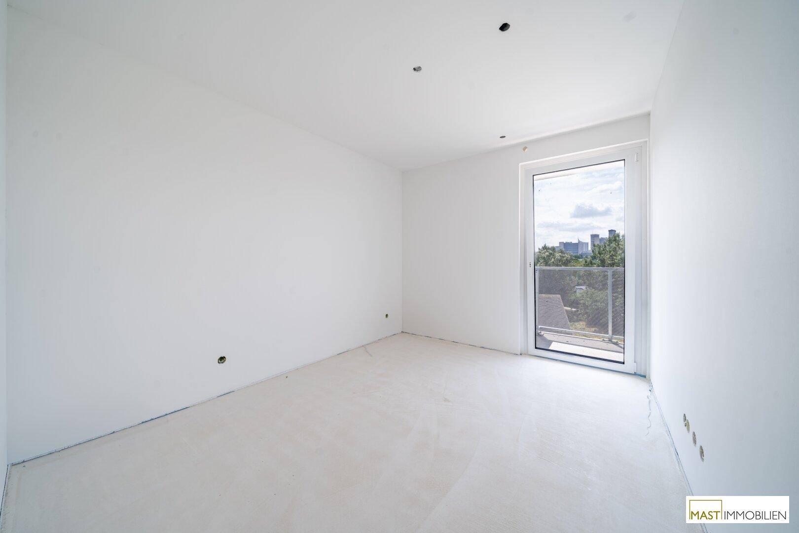 Unmöbliertes Zimmer im Rohbau mit Fenster und Zugang zu einem französischen Balkon.